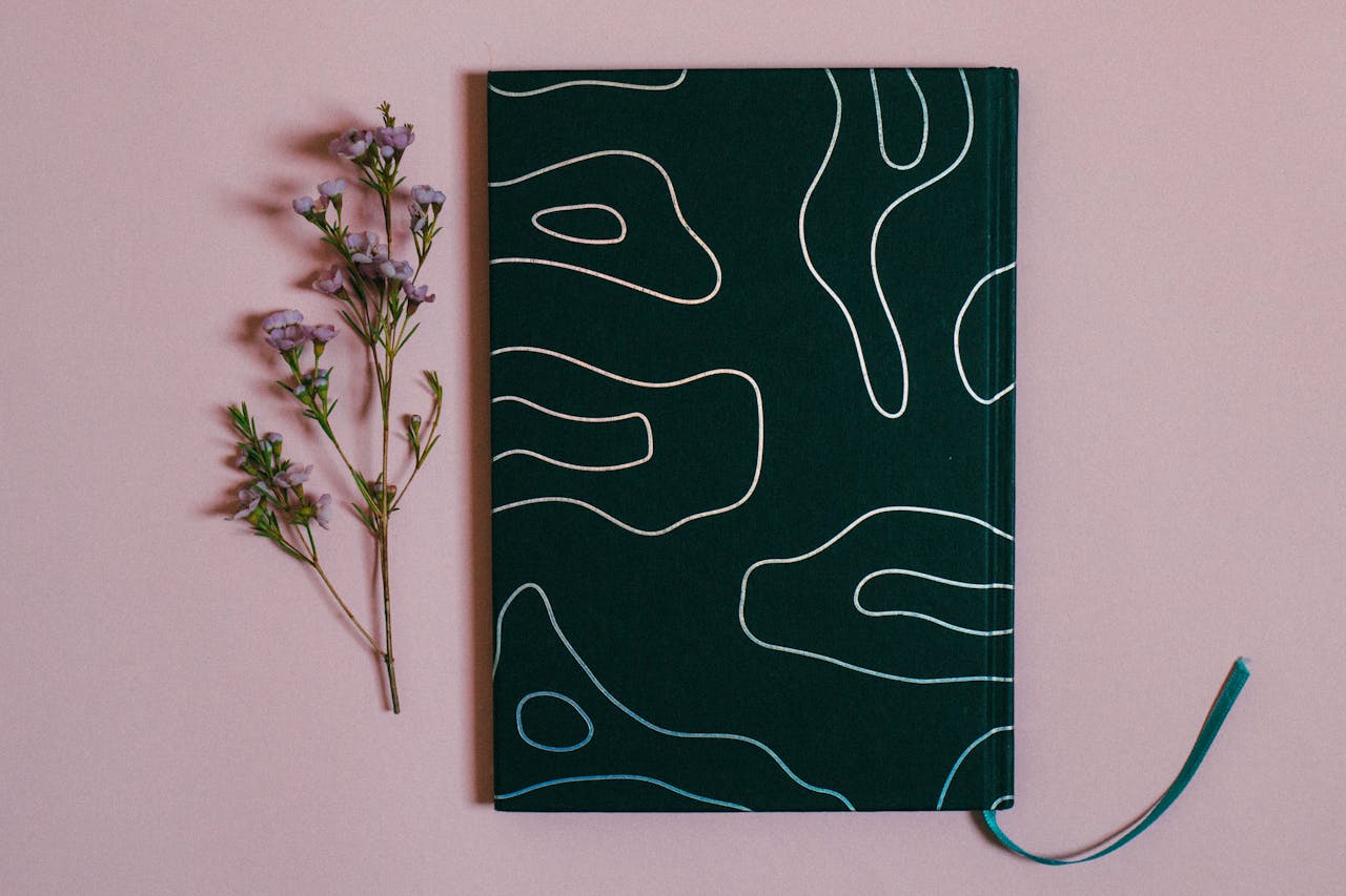 Stylish dark green notebook paired with delicate flowers on a pastel background, perfect for creatives.